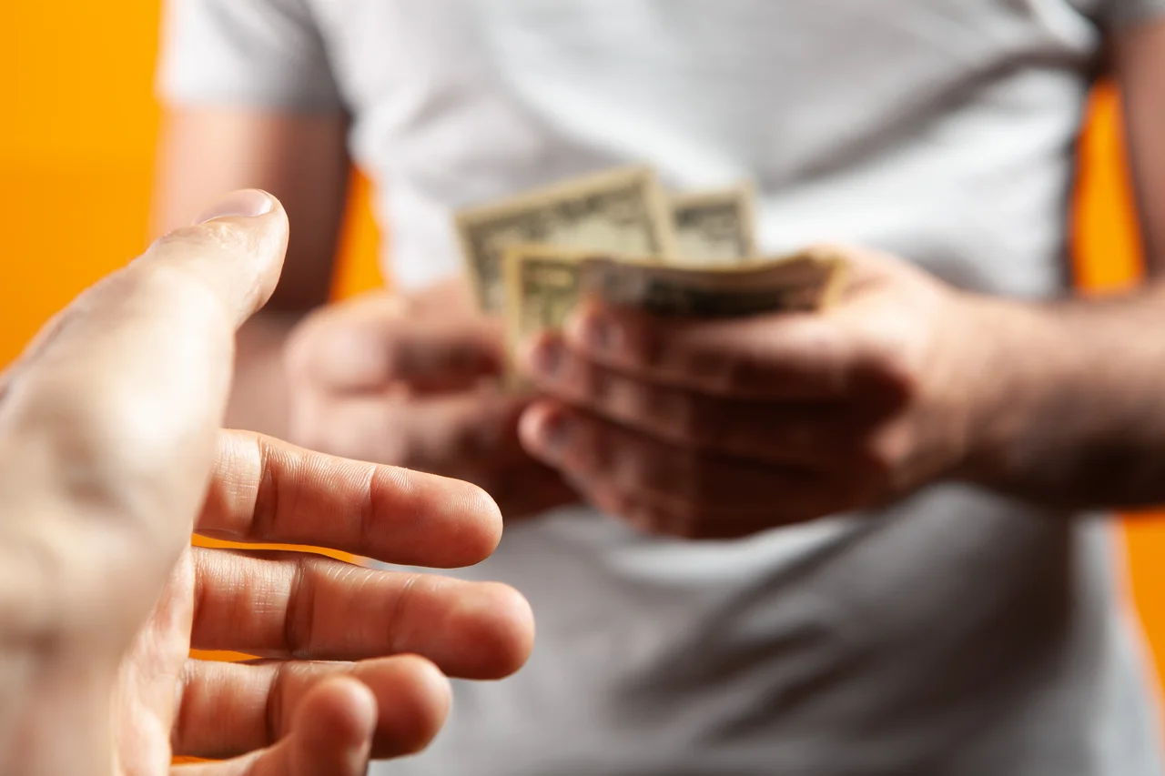 Hombre sujetando dinero y dándole otro sobre fondo naranja